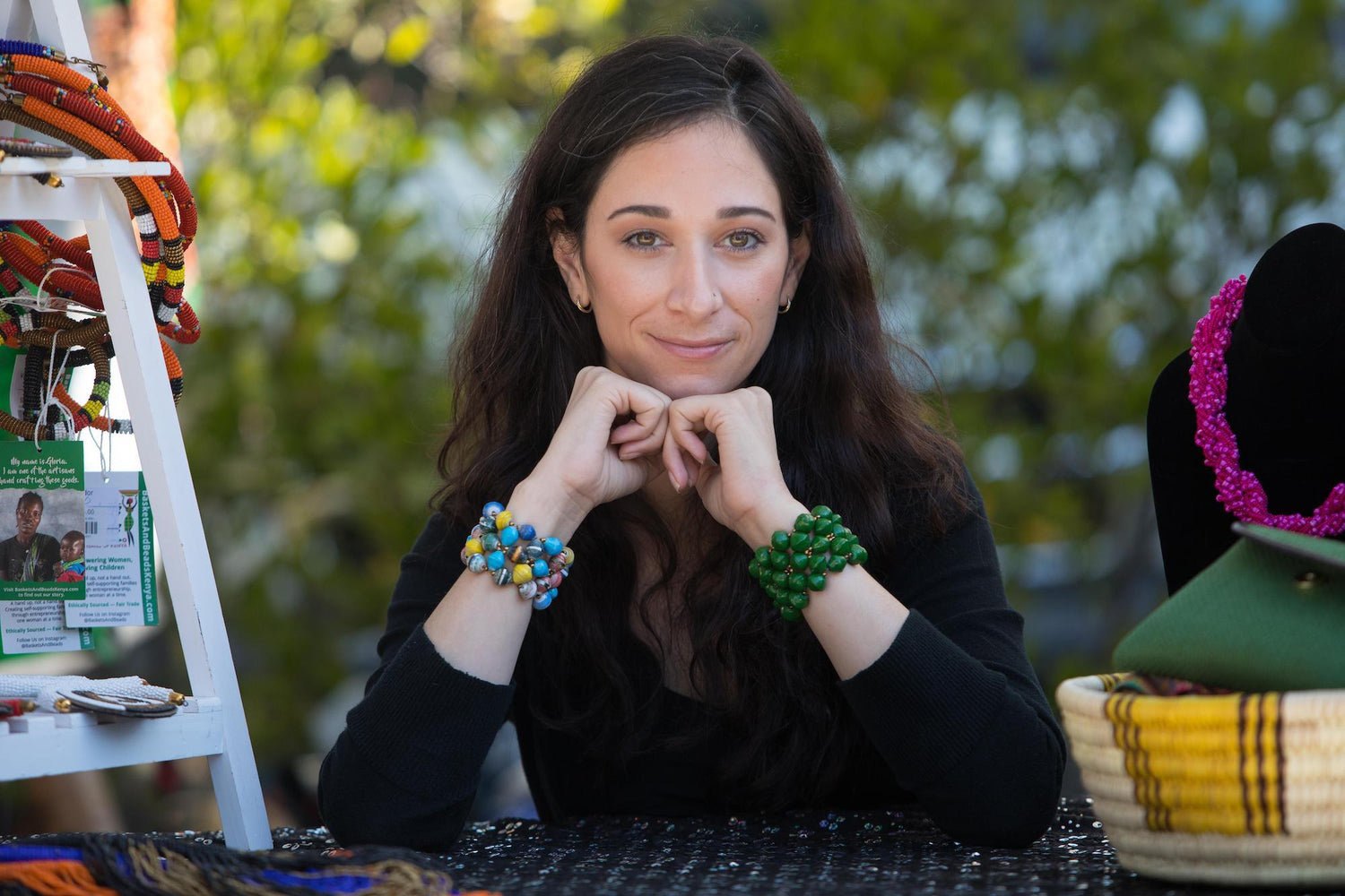 Woman leaning on a table propping her hands under her chin showing a bracelet on each arm