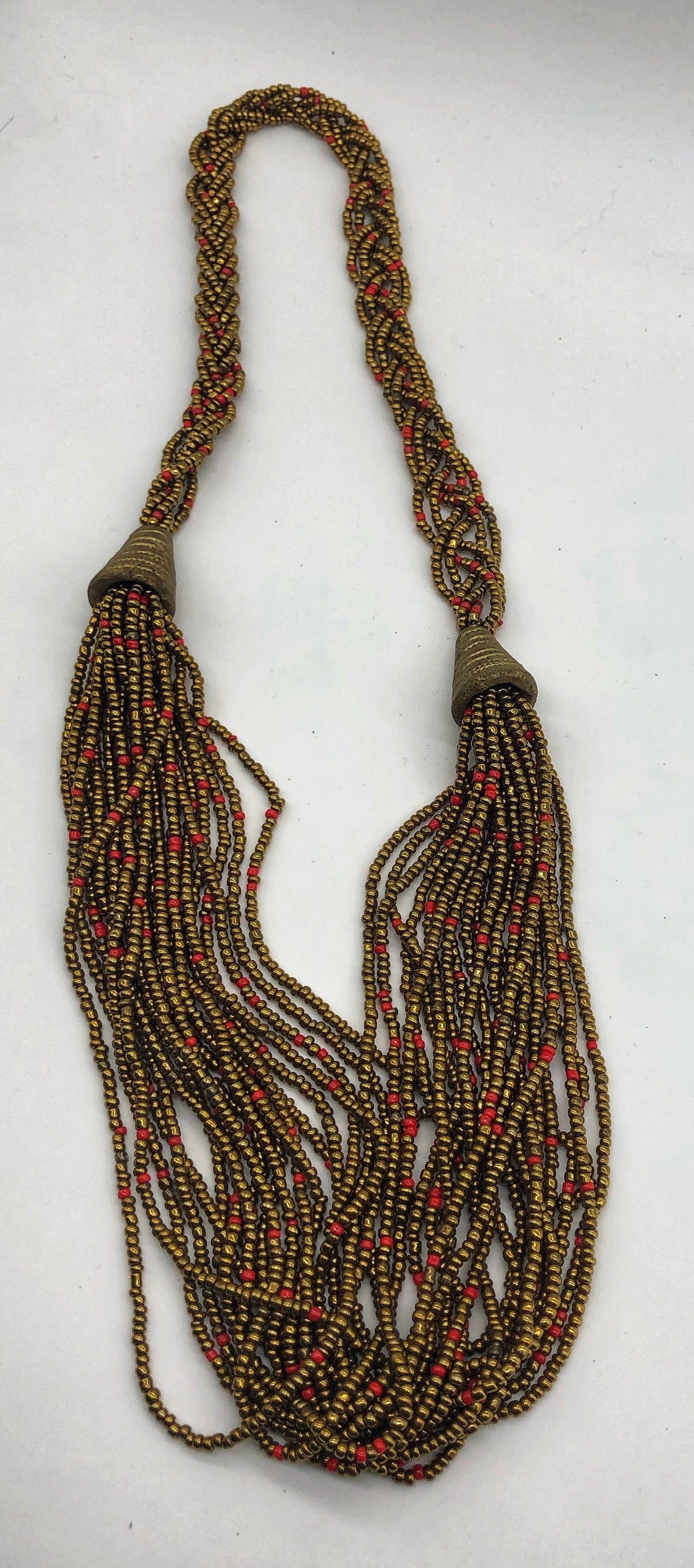 Make a statement with this beautiful handmade seed bead necklace. Styled with braided beads around the neck flowing into a loose styled design. Gold with orange bead accent