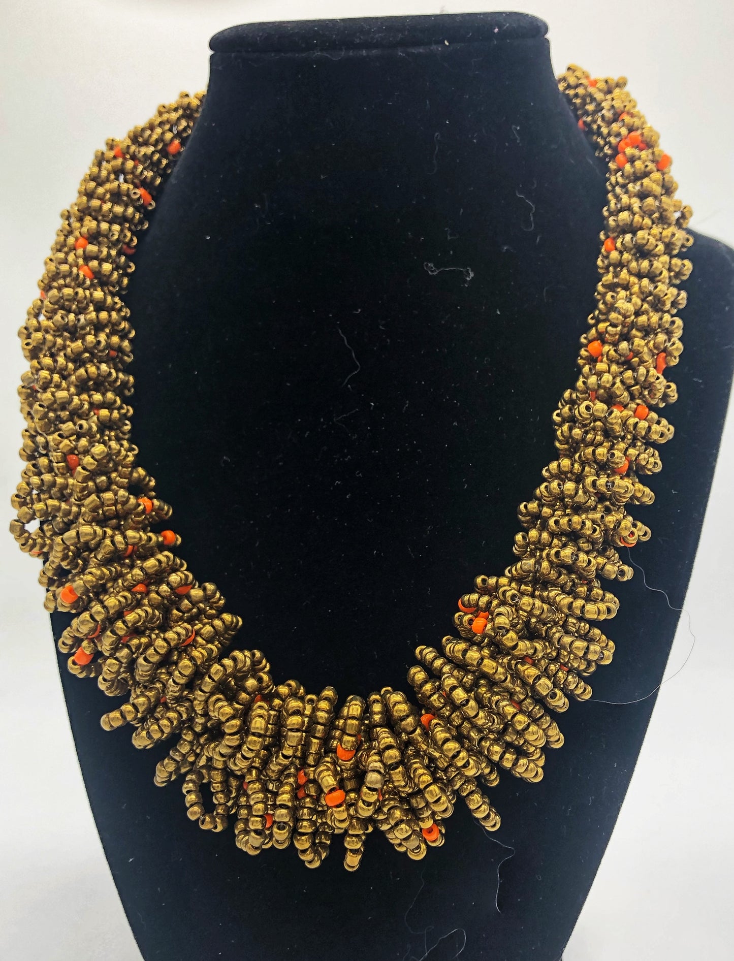 Stand out in style with this beautiful handmade loop bead style necklace. Hover over the photo to see the detail of how the beads are made into a loop design. Thoughtfully designed for style and stand out fashion. Approximately 18" end to end. Gold with orange accent beads
