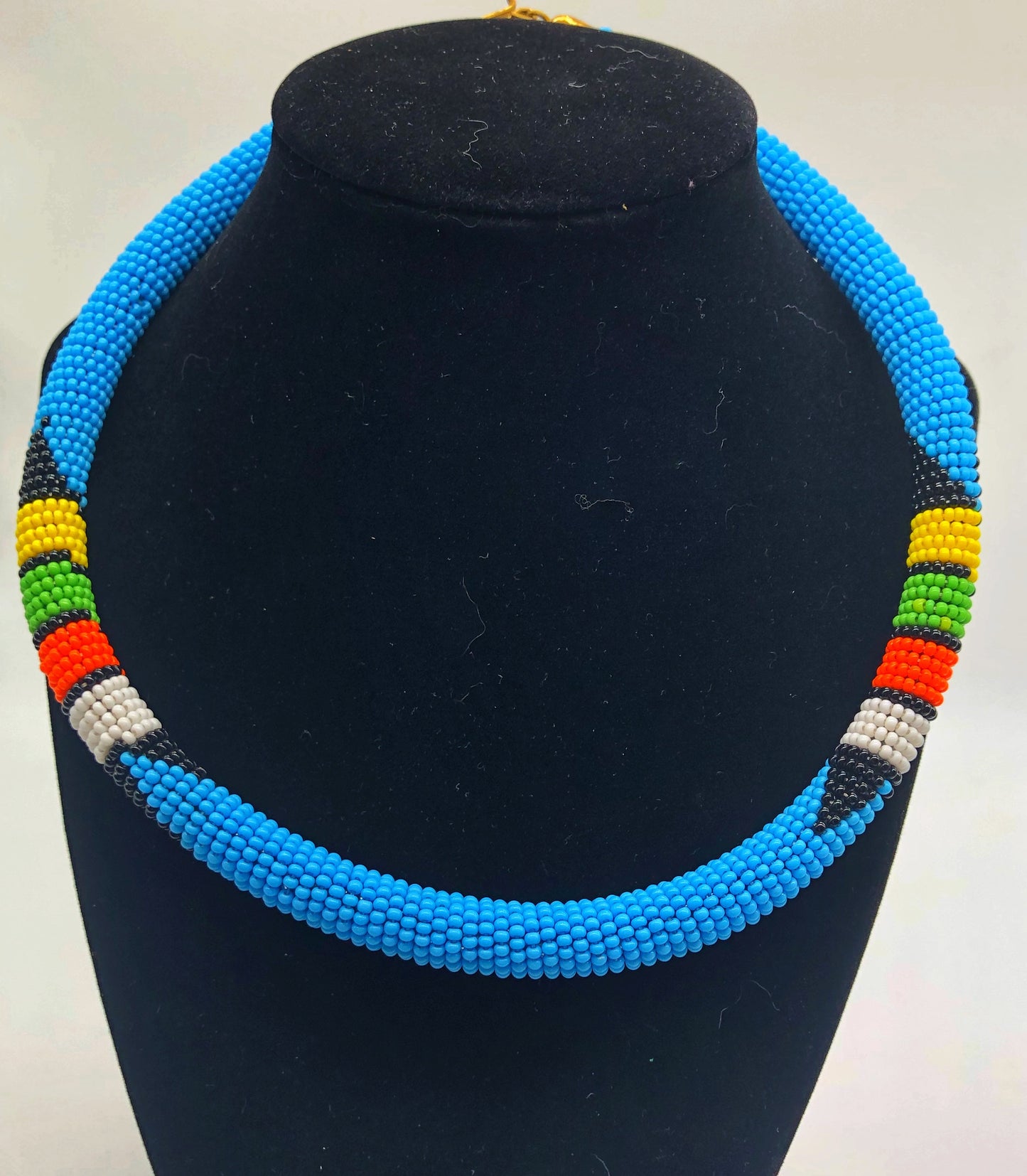 Wear the epitome of Kenya style with The Bintiah necklace. This necklace is handmade using colorful seed beads that are intricately and tightly wrapped around a solid piece fo make a stunning statement with any outfit. Multiple colors pictured. Light blue with colorful bead accend.