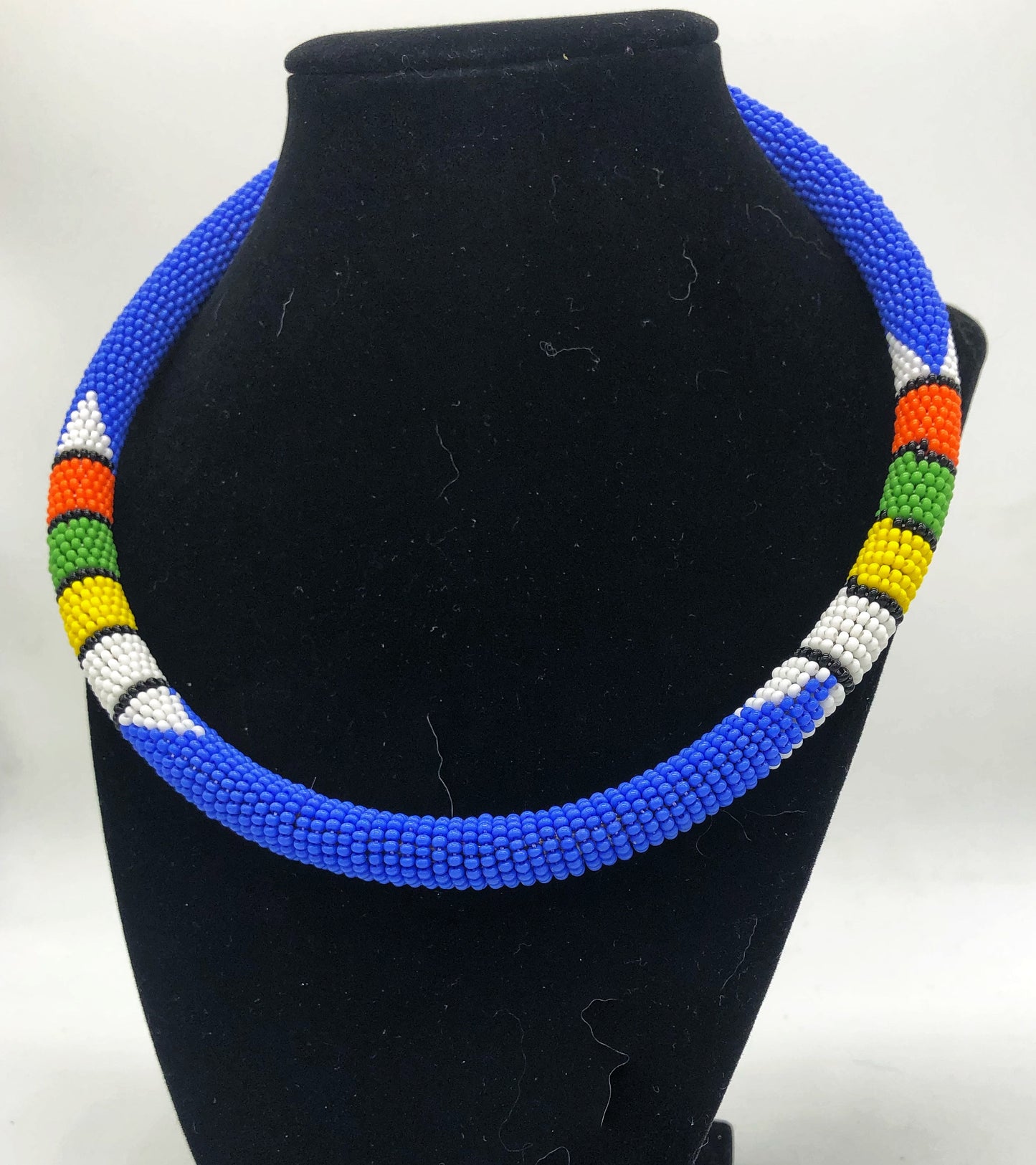 Wear the epitome of Kenya style with The Bintiah necklace. This necklace is handmade using colorful seed beads that are intricately and tightly wrapped around a solid piece fo make a stunning statement with any outfit. blue with colorful bead accent