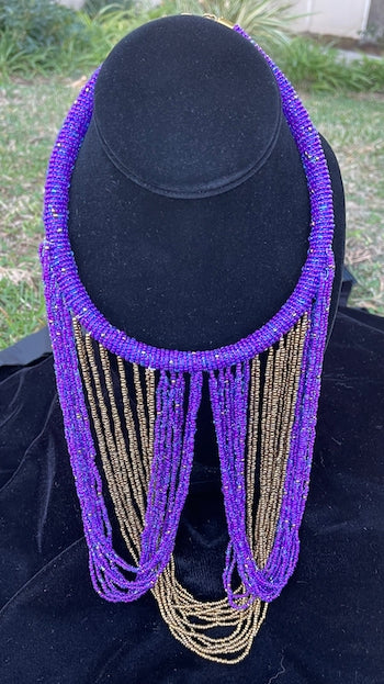 Purple and gold necklace hanging on bust. Chocker with long strands of purple and gold beads hanging down and looping back to connect to choker.