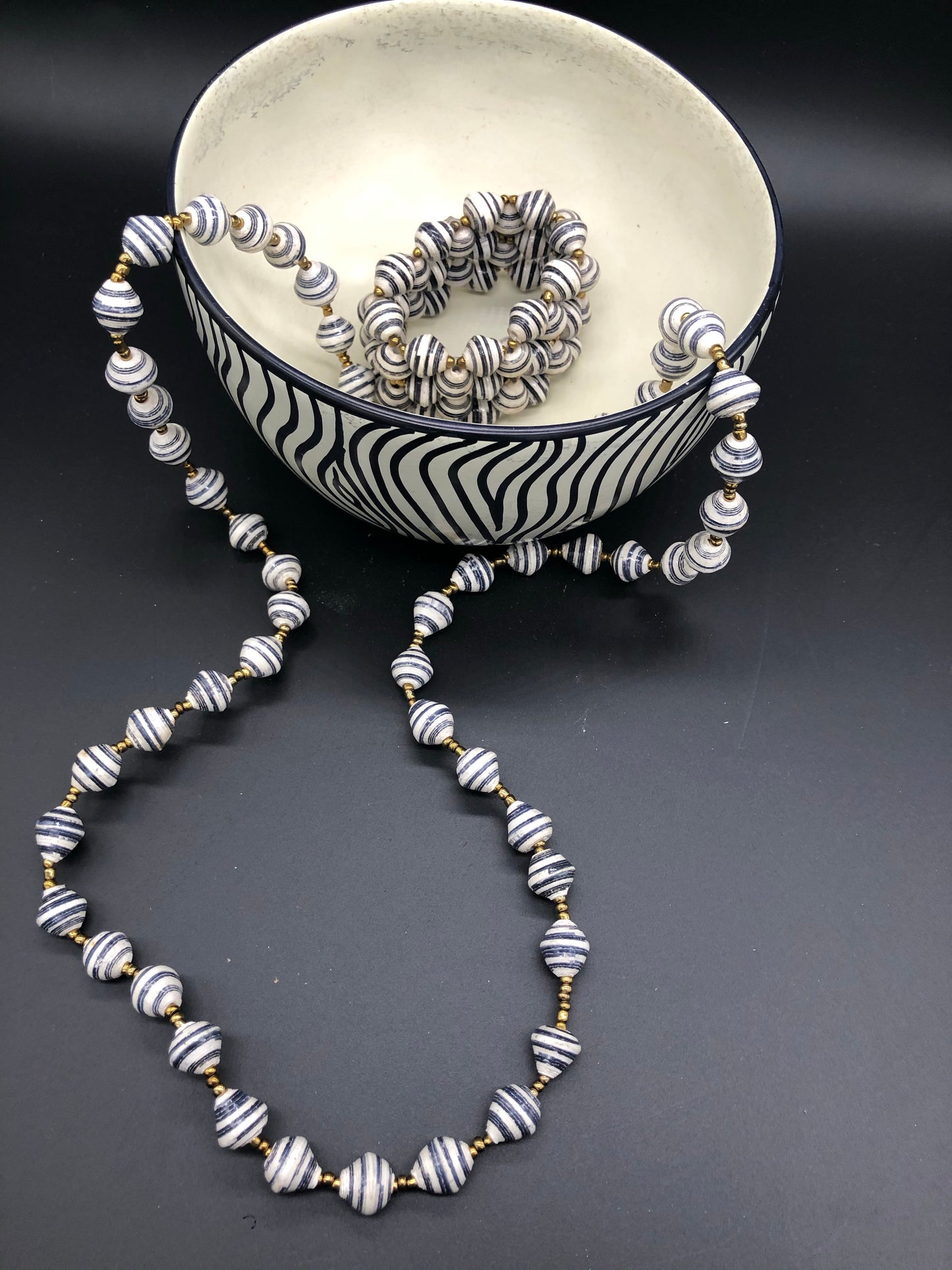Hand crafted medium length black and white paper bead necklace and stretch bracelet set. Necklace approximately 18 inches long. Pattern is narrow white with black accent paper bead made from magazines. Each bead individually rolled by hand. Stylish and Fashionable for casual or dressy. Fair trade.