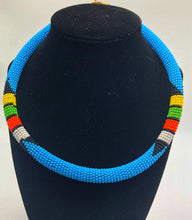 Load image into Gallery viewer, Wear the epitome of Kenya style with The Bintiah necklace.  This necklace is handmade using colorful seed beads that are intricately and tightly wrapped around a solid piece fo make a stunning statement with any outfit.  Multiple colors pictured. Light blue with colorful bead accend. 
