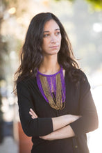 Load image into Gallery viewer, Model from waist up in black with long dark brown hair wearing Mary beaded purple and gold necklace. Chocker style necklace with long strands of purple and gold beads hanging down to breast area.  Loops down and back up to chocker to connect. 