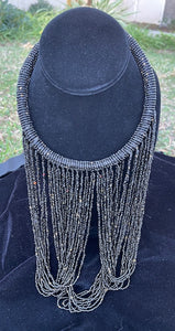 Black necklace hanging on bust. Chocker with long strands of black beads hanging down and looping back to connect to choker.