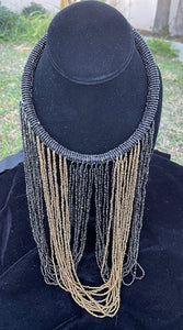 Black and gold necklace hanging on bust. Chocker with long strands of black and gold beads hanging down and looping back to connect to choker.