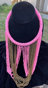 Pink and gold necklace hanging on bust. Chocker with long strands of pink and gold beads hanging down and looping back to connect to choker.