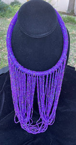 Purple necklace hanging on bust. Chocker with long strands of purple and gold beads hanging down and looping back to connect to choker.
