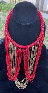 Red and gold necklace hanging on bust. Chocker with long strands of red and gold beads hanging down and looping back to connect to choker.
