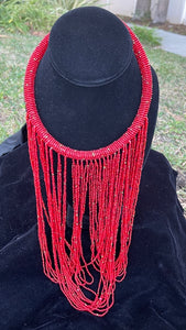 Red necklace hanging on bust. Chocker with long strands of red beads hanging down and looping back to connect to choker.
