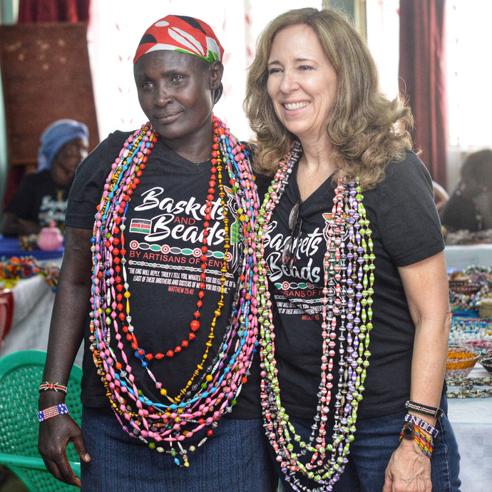 2 women standing and wearing strands of long paper beads in multiple colors also wearing baskets and beads t-shirts 