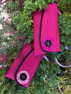 2 Hot Pink clutches round bead embellishment and black piping on flap laying on green plants
