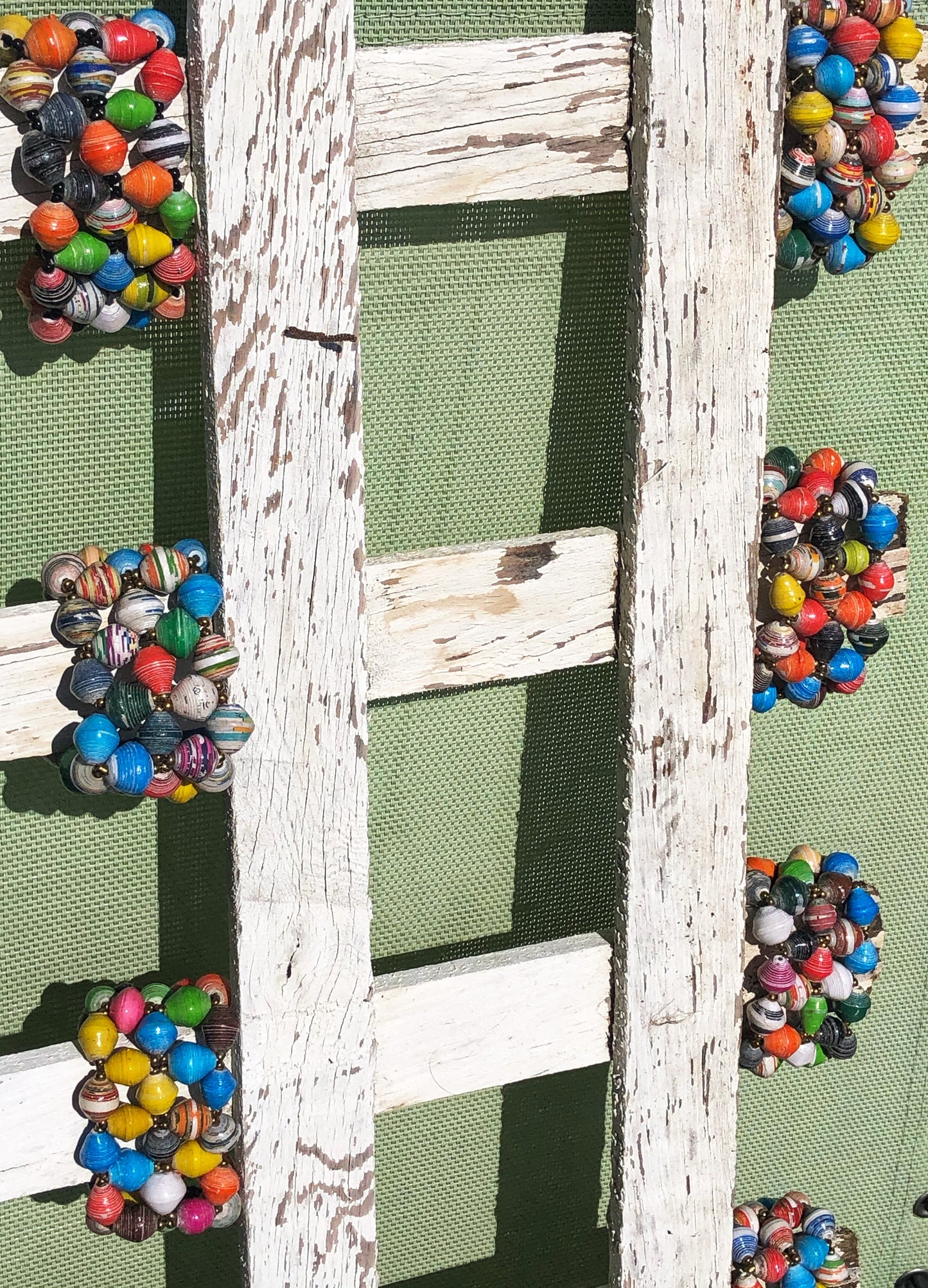 White wooden short fencing standing sideways with a multi color paper bead bracelet on each rung 