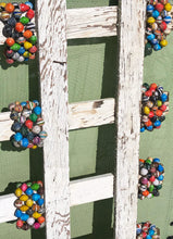 Load image into Gallery viewer, White wooden short fencing standing sideways with a multi color paper bead bracelet on each rung 